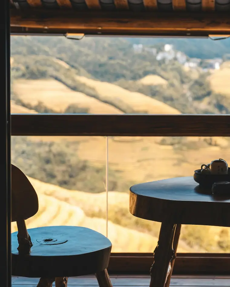 A woman sitting at a wooden table overlooking green terraced hills