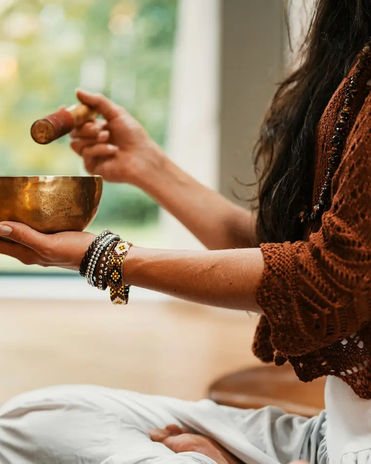 Hands holding a brass singing bowl and striker, with soft incense smoke
