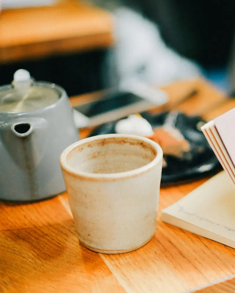 Hands opening a notebook beside a cup of coffee on a wooden table